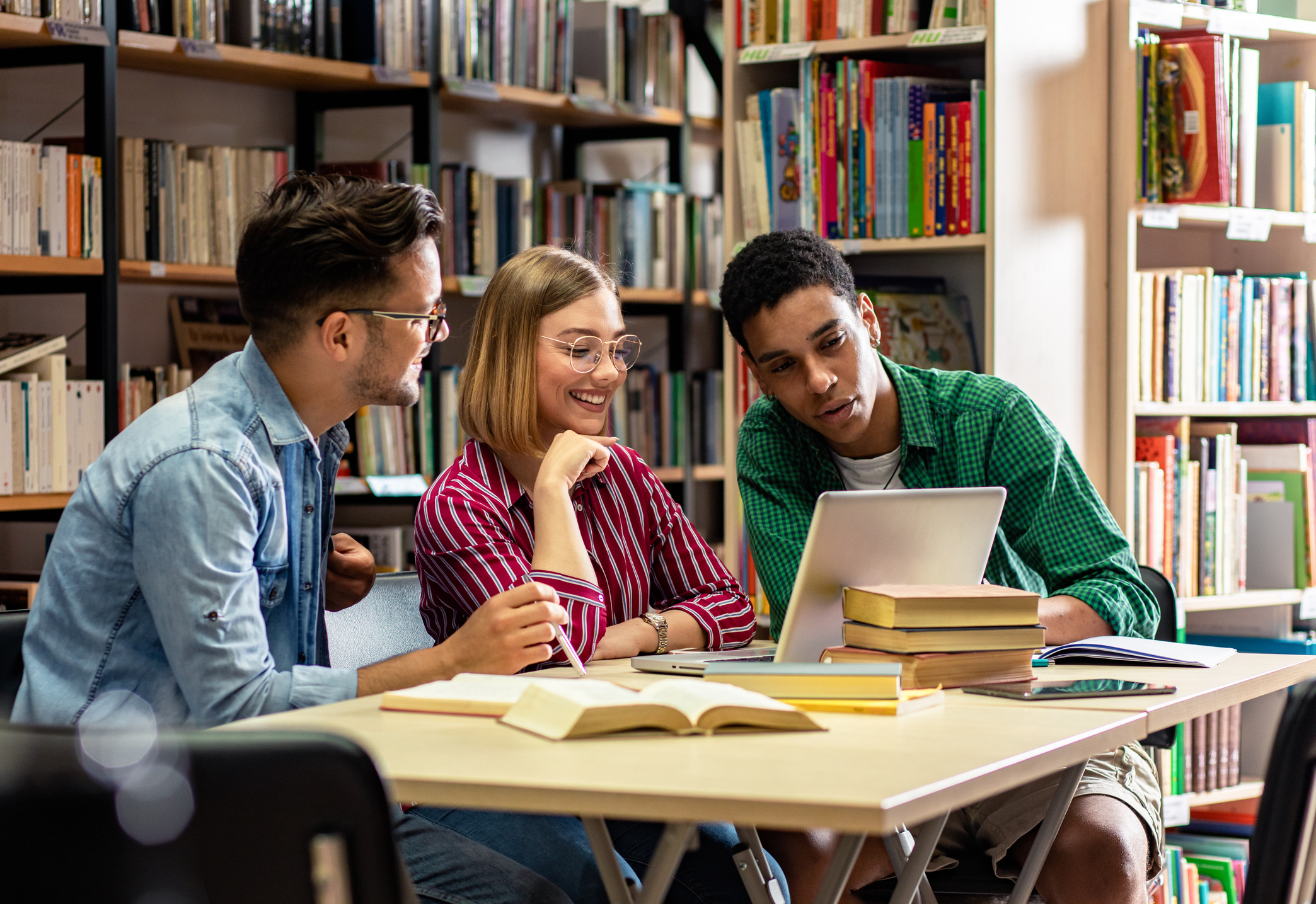 Three young students study in the school library and using laptop for researching online.