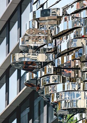 Close-up of the kinetic sculpture "Head of Franz Kafka" in motion. One can see the different bright metal planes of the sculpture reflecting scenery in front of the slightly blurred background of an office building