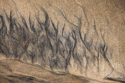 Beach sediment forming small braided rivers in the surf zone with dark minerals differentiated by their specific weight, Northern Algarve, Portugal